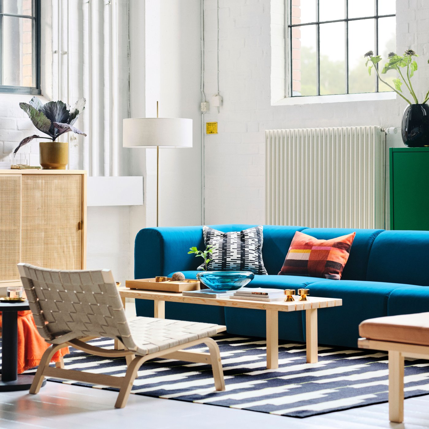 A living room with a dark turquoise STOCKHOLM 2025 4-seat sofa, easy chairs, and a floor lamp arranged around a coffee table.