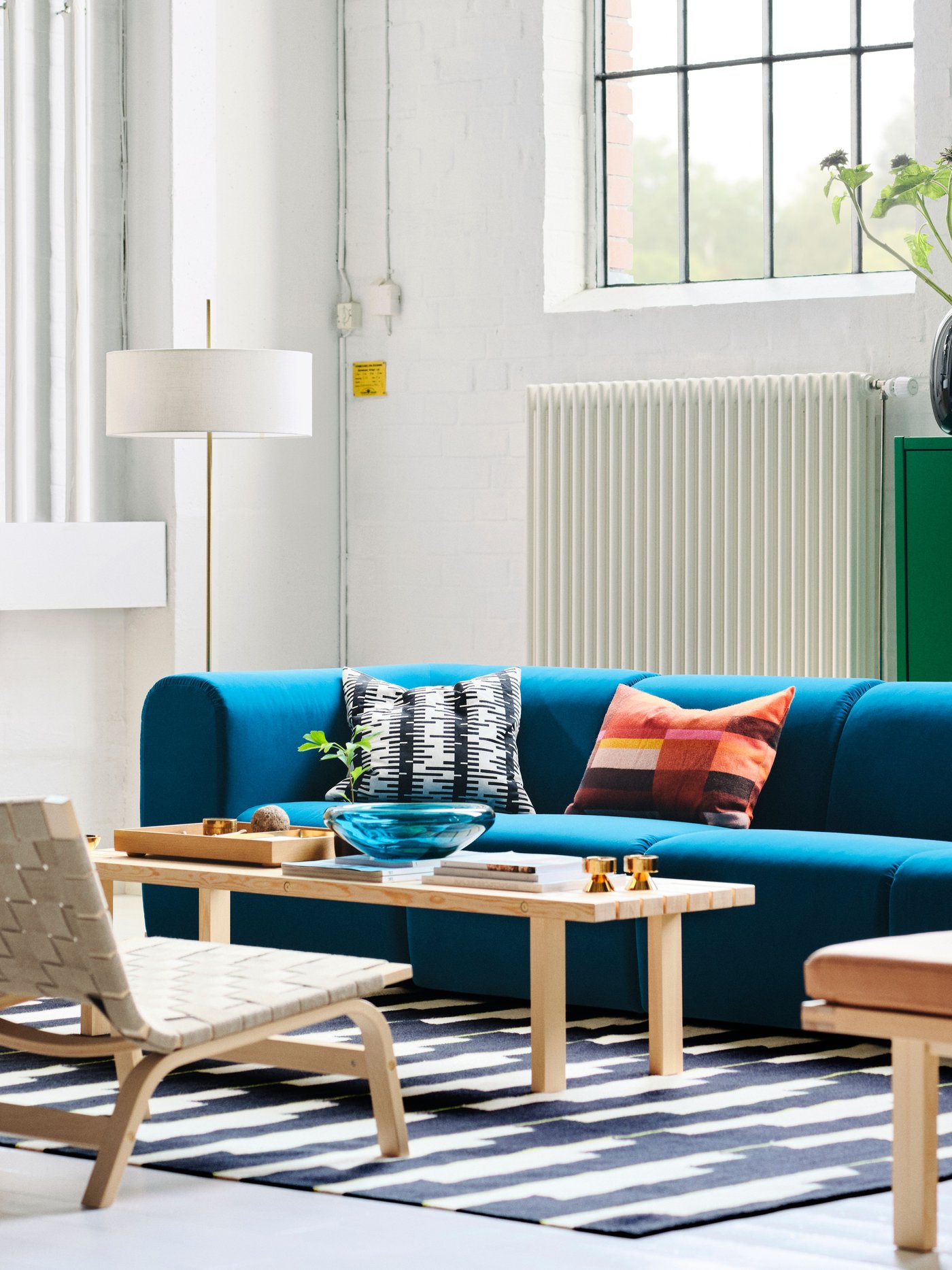 A living room with a dark turquoise STOCKHOLM 2025 4-seat sofa, easy chairs, and a floor lamp arranged around a coffee table.