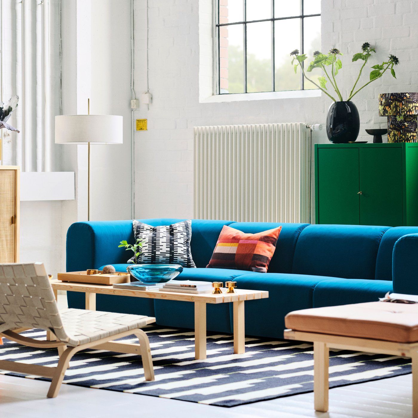 A living room with a dark turquoise STOCKHOLM 2025 4-seat sofa, easy chairs, and a floor lamp arranged around a coffee table.