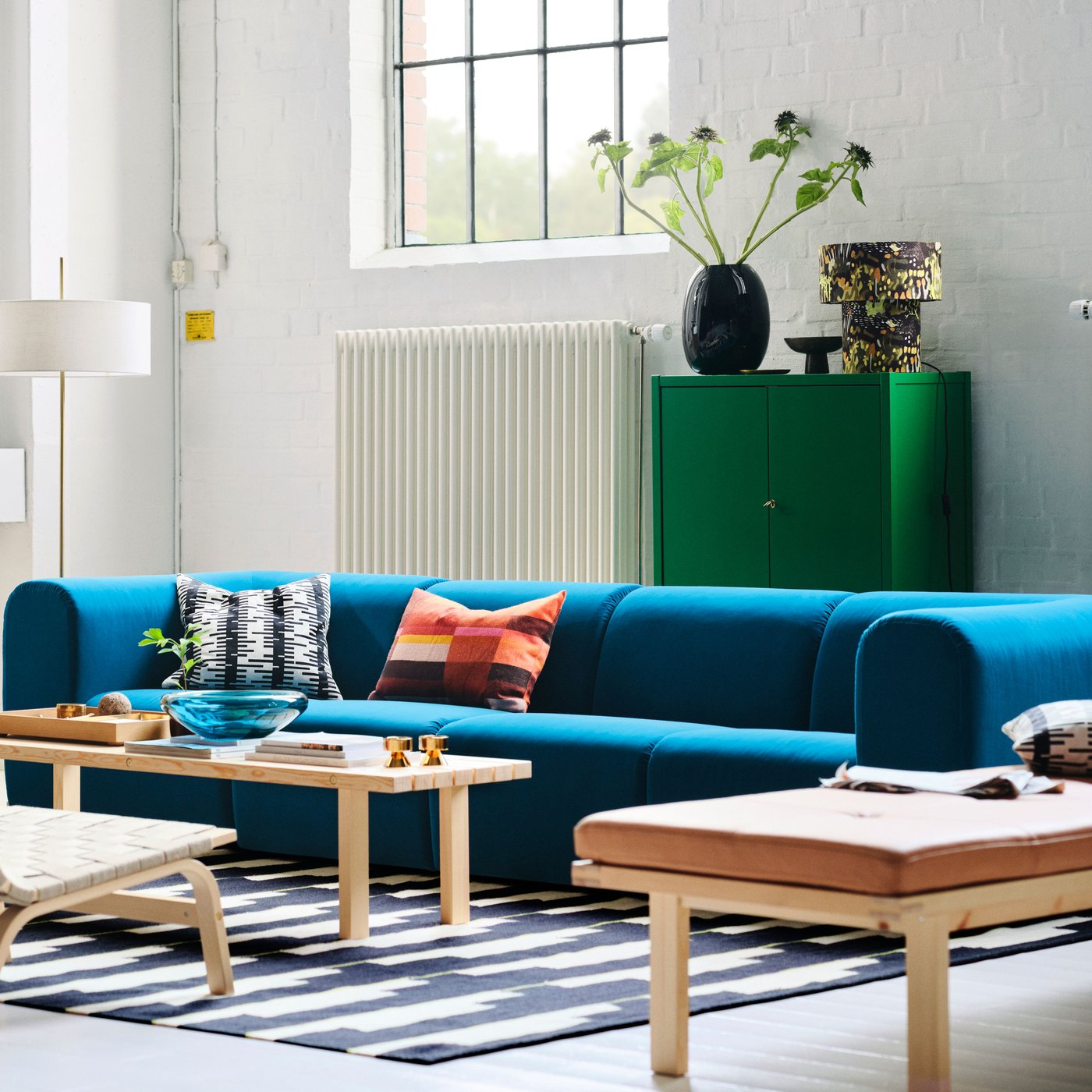 A living room with a dark turquoise STOCKHOLM 2025 4-seat sofa, easy chairs, and a floor lamp arranged around a coffee table.