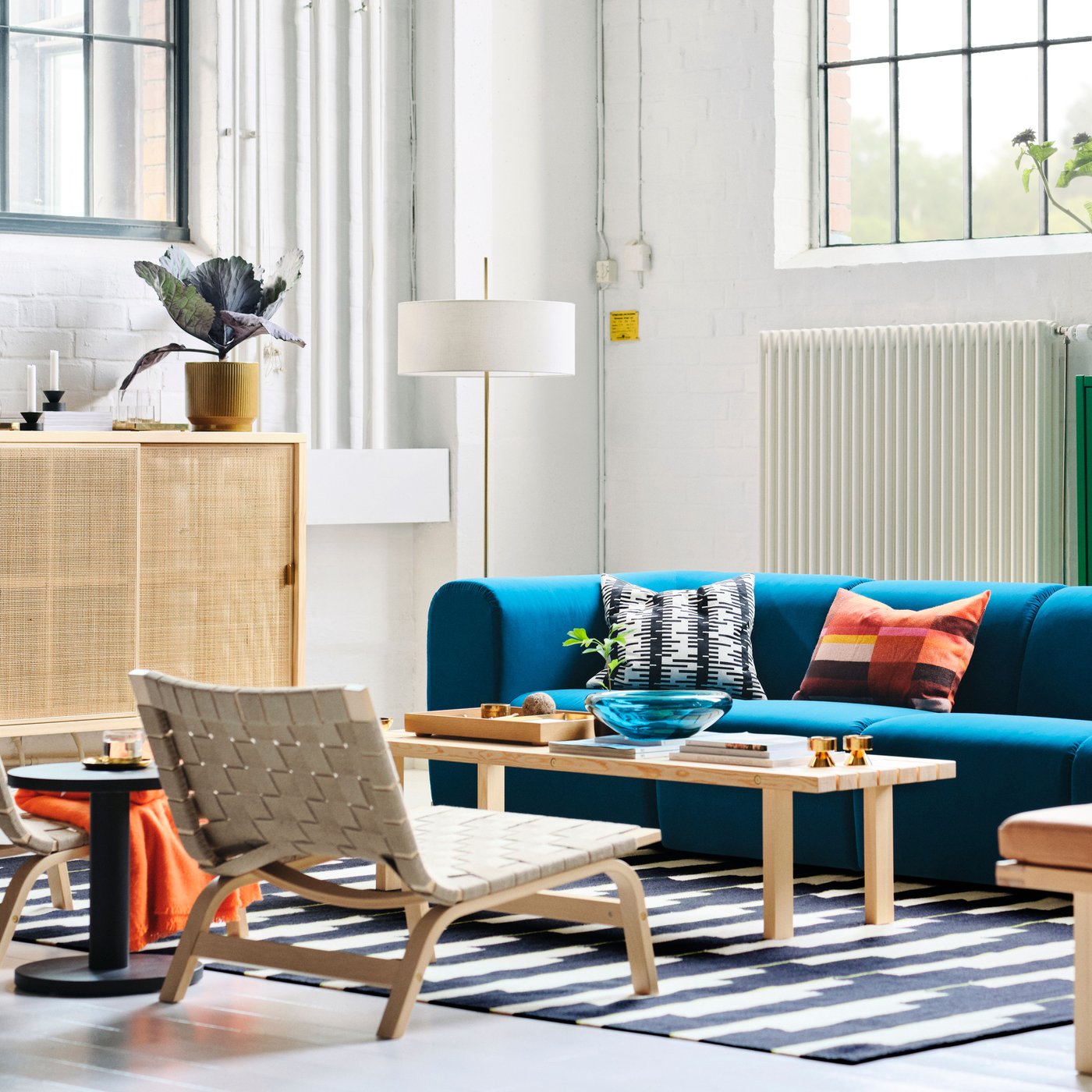 Unha sala cun sofá STOCKHOLM 2025 turquesa escuro de 4 prazas, unha lámpada de pé e cadeiras de brazos dispostas arredor dunha mesa de centro.