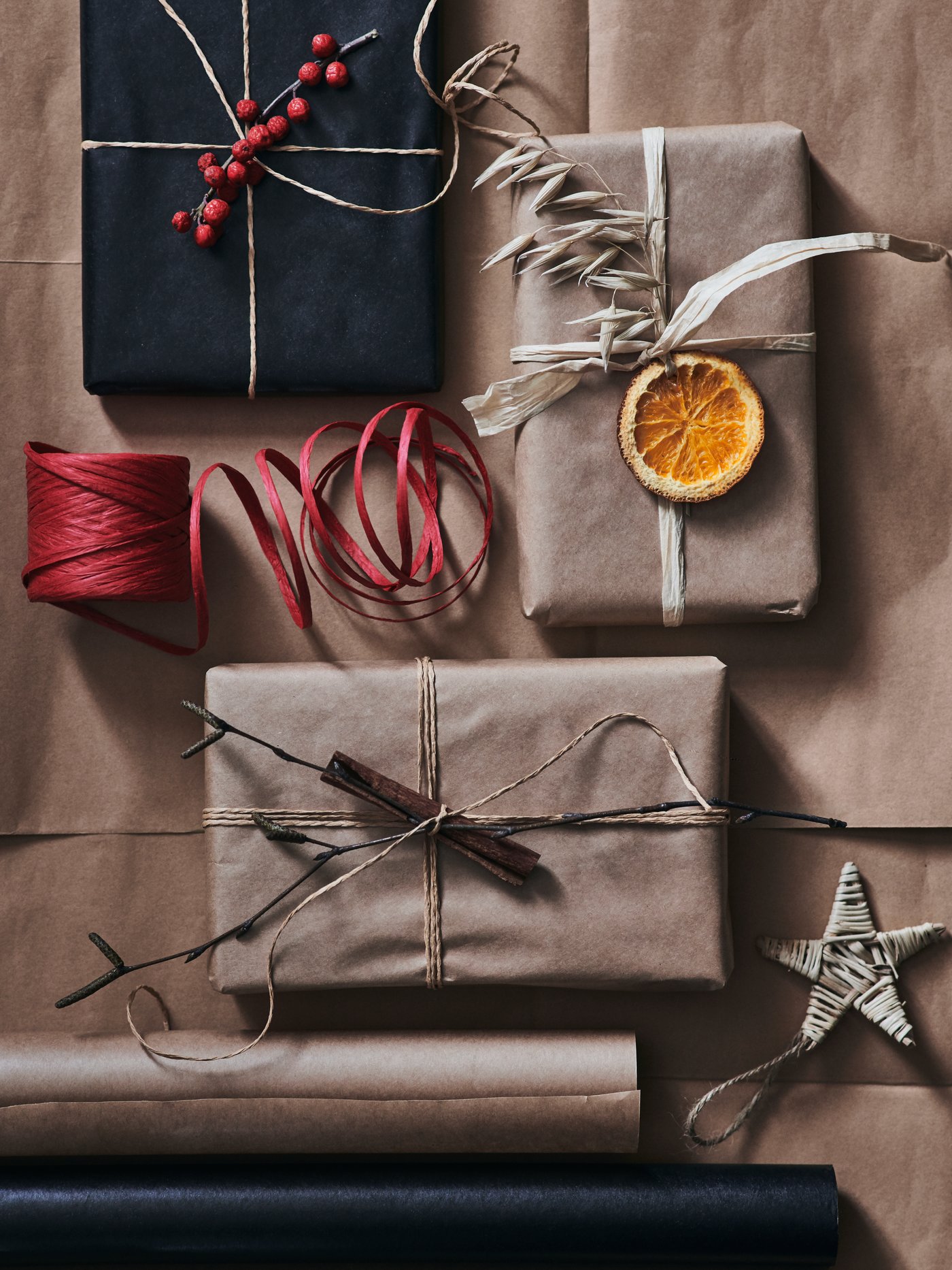 Verschiedene Geschenke in Geschenkpapier aus reinem Papier. Dekoriert sind sie mit Gräsern, getrockneten Orangenscheiben und ein paar Zimtstangen.