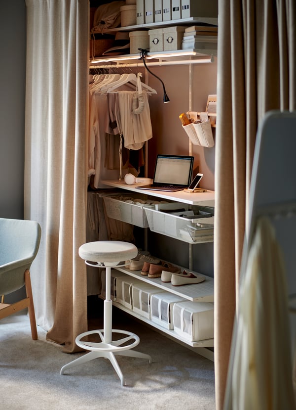 A BOAXEL wardrobe combination, partly screened off by beige ANNAKAJSA curtains, used as a workstation and to store clothes.