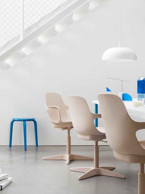 Un espace de travail équipé d’un long bureau blanc, de trois chaises pivotantes beiges, d’une suspension blanche, de décorations bleues et d’un tabouret assorti.