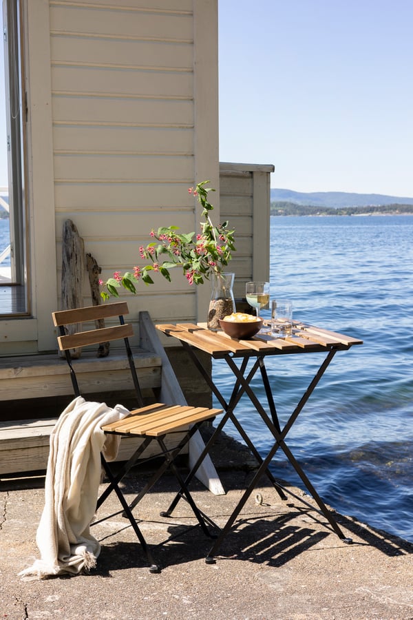 Cafëset med bord och stol framför en vit sommarstuga med havet i bakgrunden.