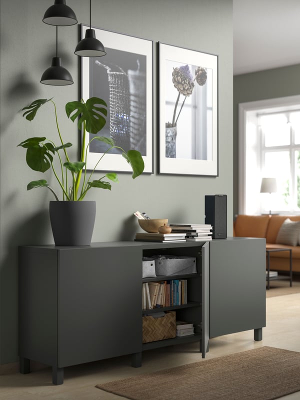 A BESTÅ storage unit with LAPPVIKEN dark grey doors. On top of the cabinet is a post with a plant and some decorations.