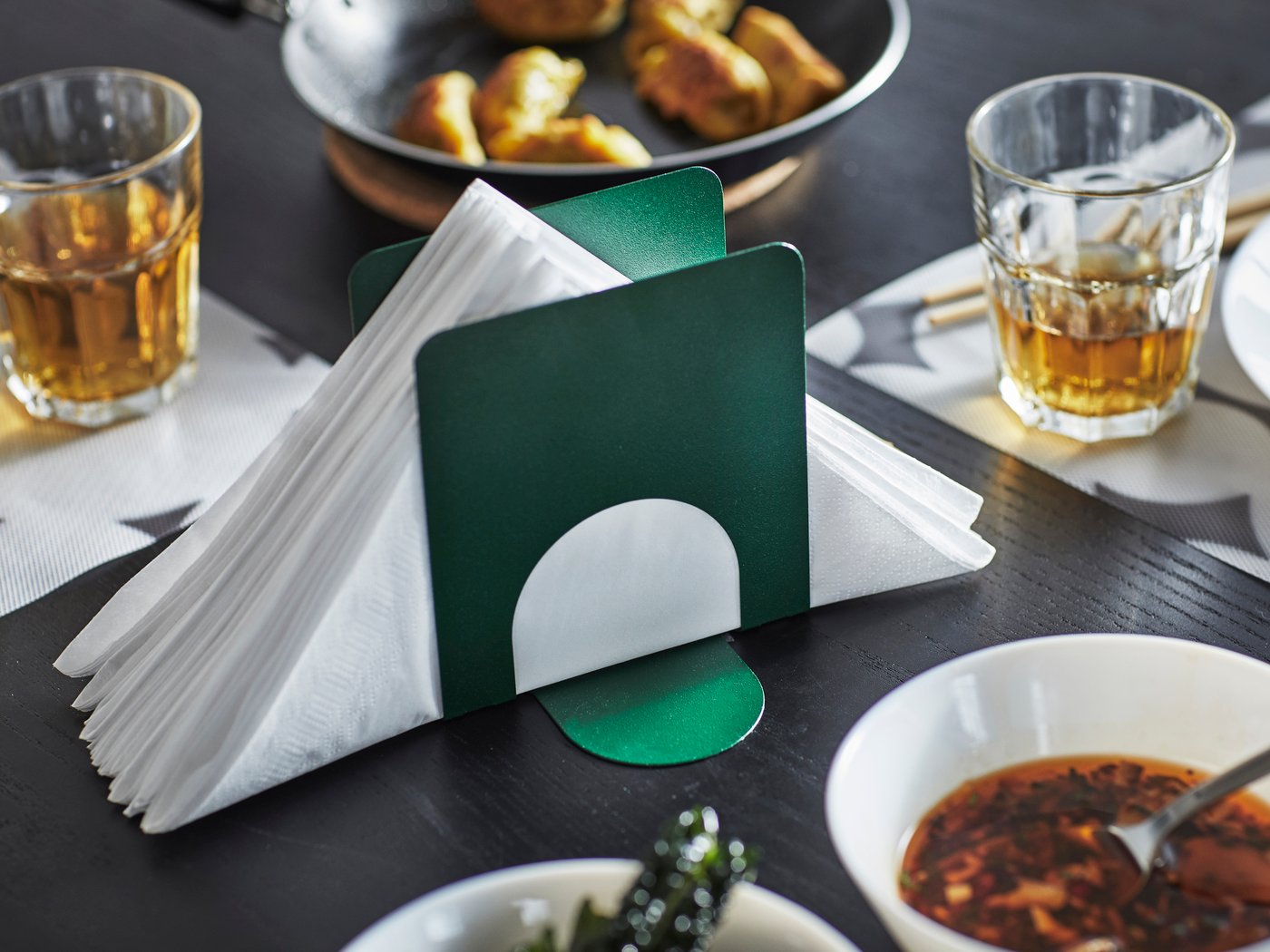 Un portatovaglioli SKOGSRÖR verde scuro in mezzo a una tavola preparata.