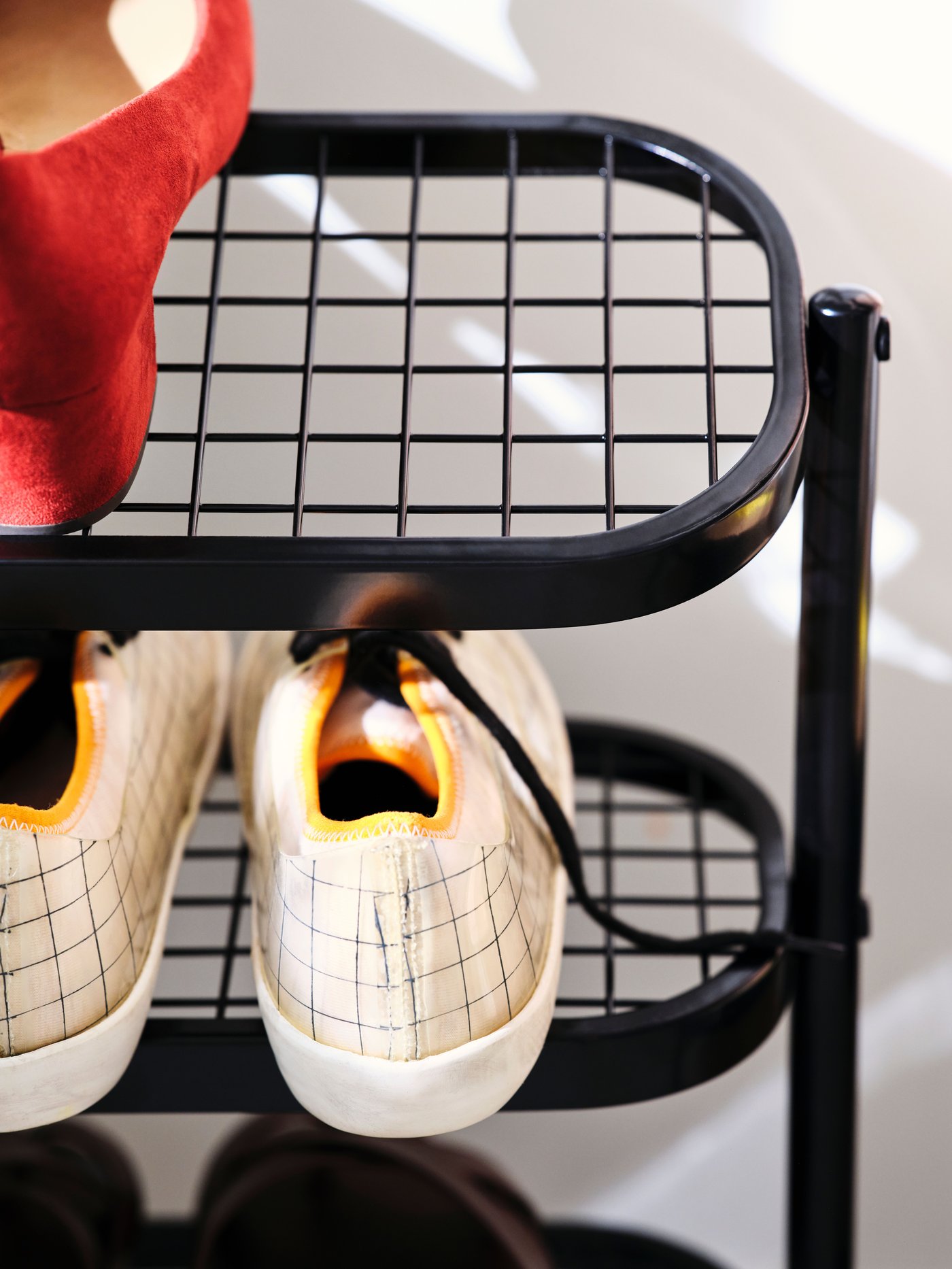 One side of a black ÄLGANÄS shoe rack with a pair of trainers on the middle shelf and a pair of red shoes on the top shelf.