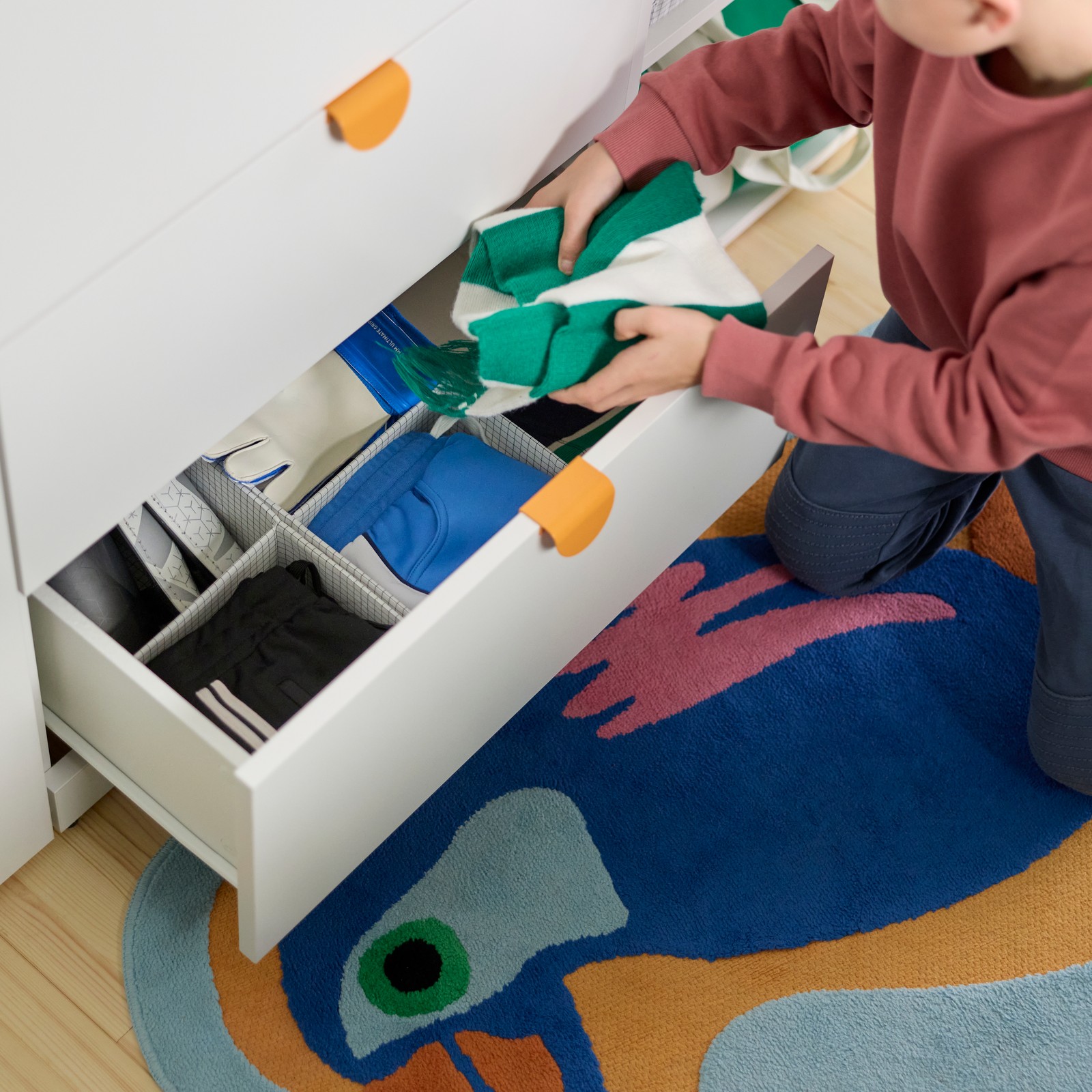 A child is sitting next to a LASTARE storage combination putting clothes into STUK boxes with compartments.