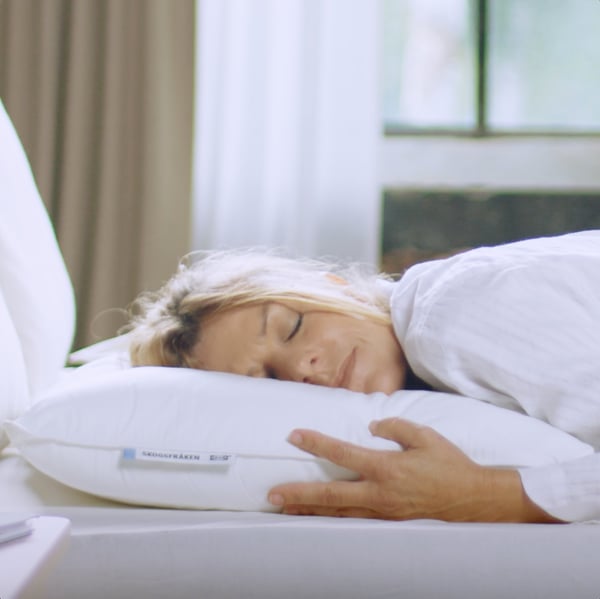 A person asleep on their stomach with their head on a SKOGSFRÄKEN pillow that does not have a pillowcase on it.