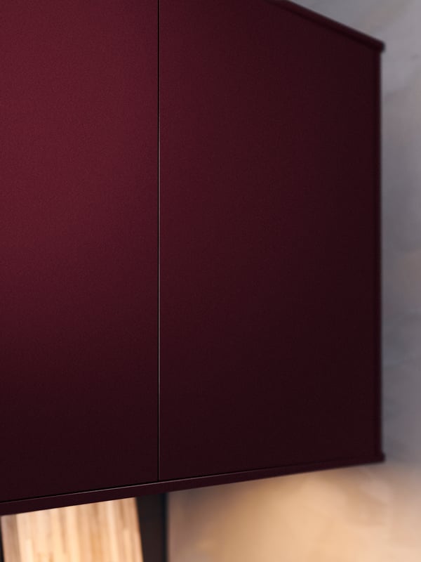 A METOD kitchen cabinet with two dark red-brown doors against a beige wall, with lighting below.
