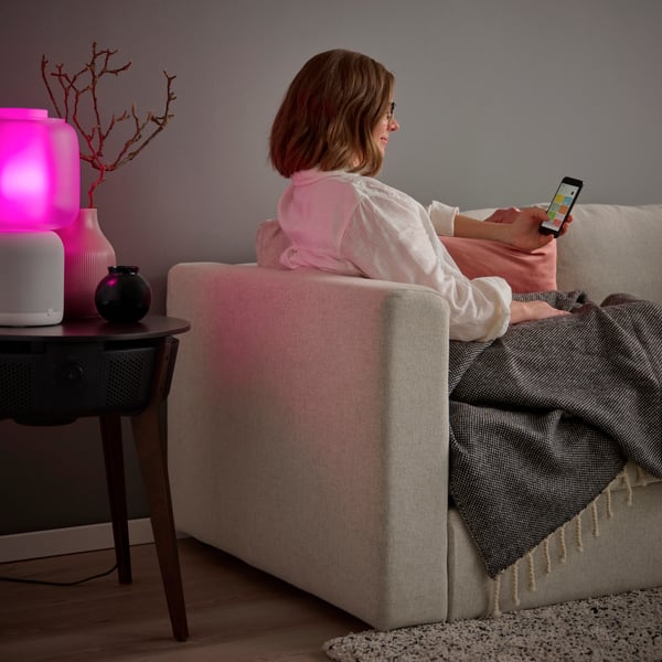 Kvinna som sitter i soffa och styr in belysningmed sin mobiltelefon.