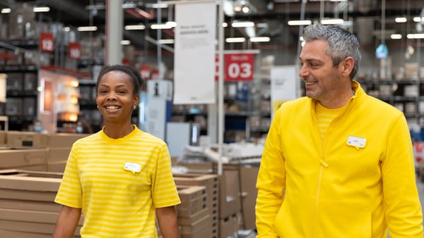 Two IKEA co-workers in yellow stood next to each other in the warehouse and smiling