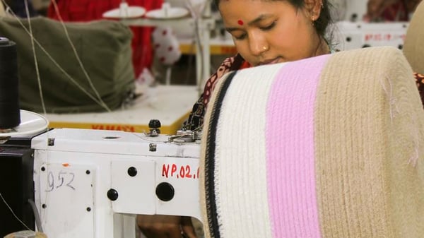 A worker operates a sewing machine, crafting a large spool of fabric with beige and pink stripes.