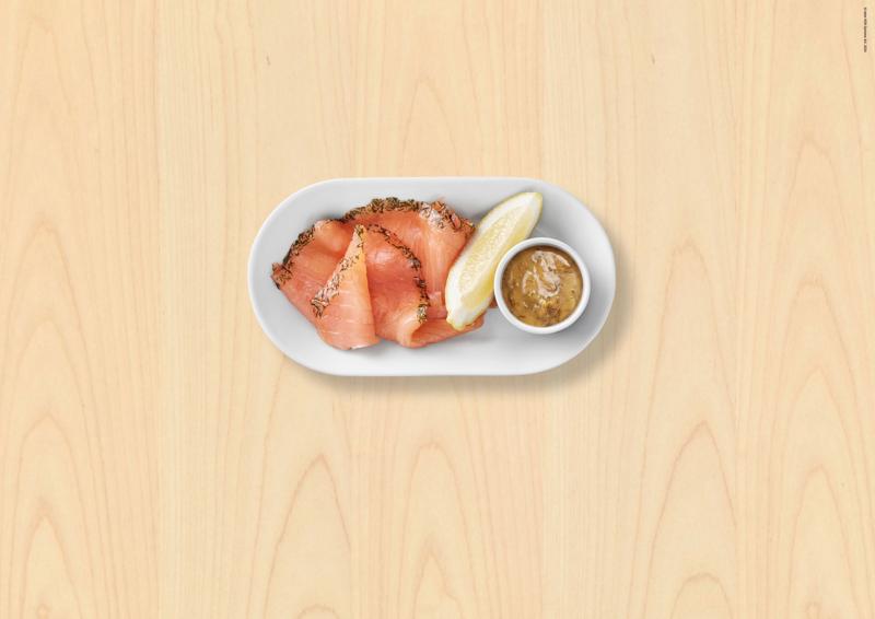 Assiette blanche avec du saumon mariné et une sauce dans un petit pot ainsi qu'un quartier de citron jaune