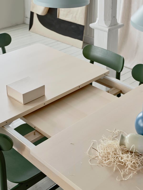 The table leaf extension lying under the table top of RÖNNINGE extendable table in light birch placed in a dining context.