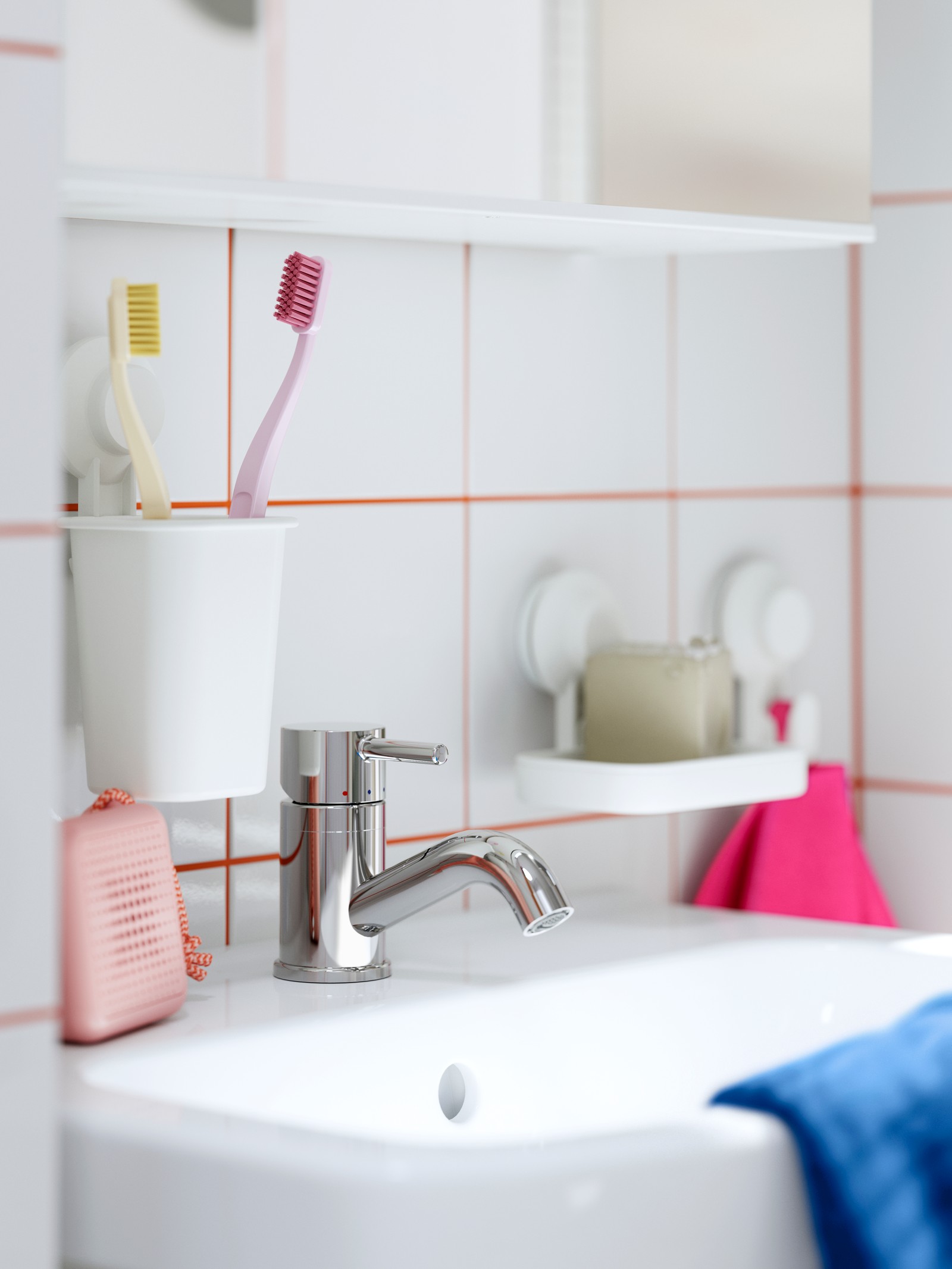 A sink with a TISKEN soap dish with suction cups, toothbrush holder, and a tap, with a pink towel hanging beside it.