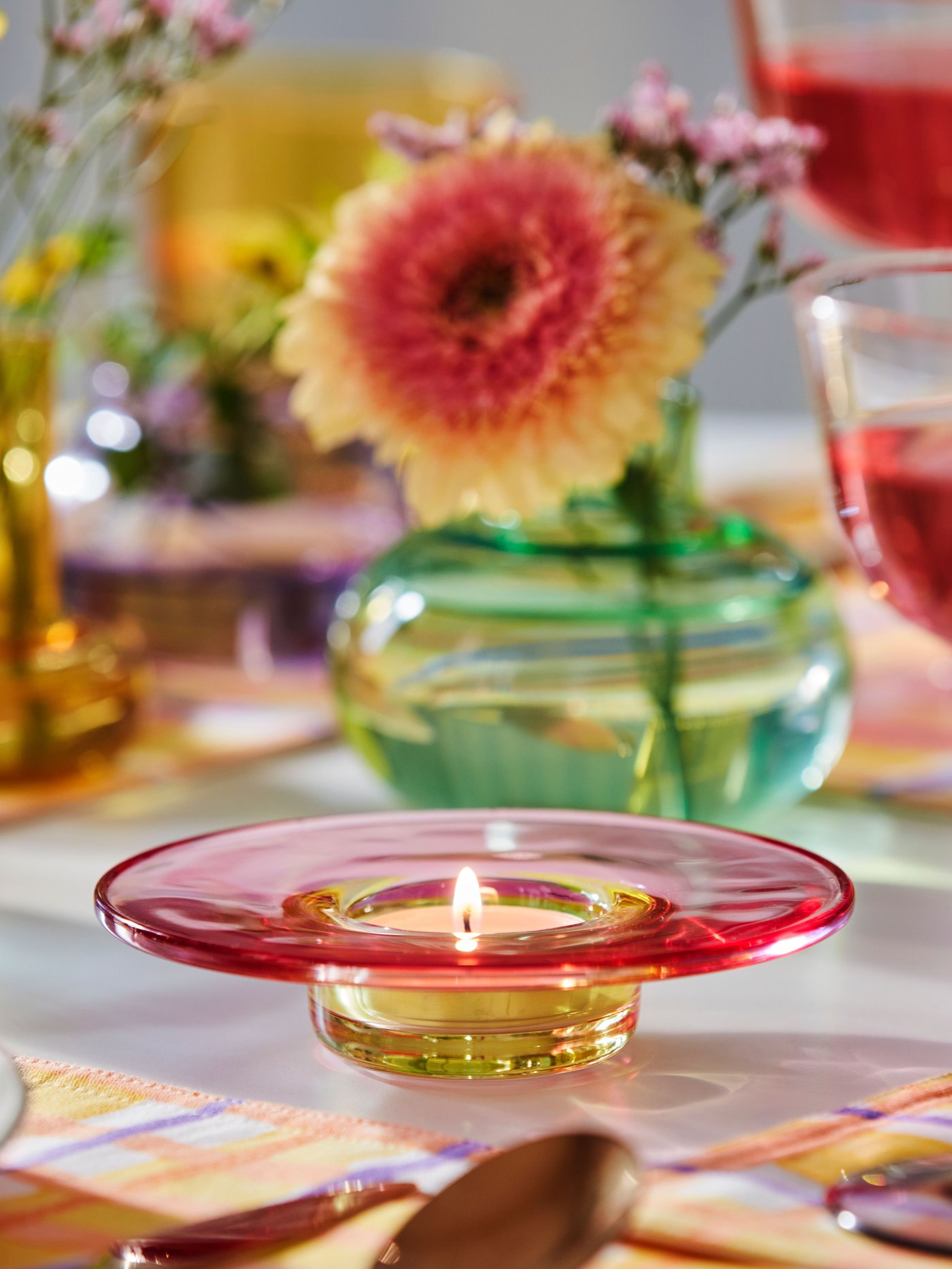 A multicoloured TJÄRLEK tealight holder with a lit tealight in the dining room.