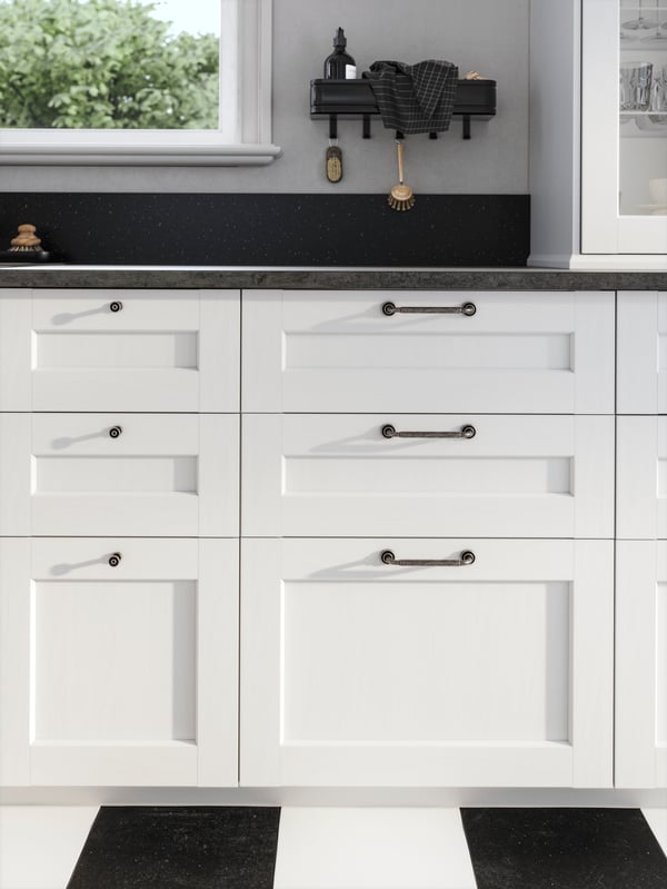 Close up of lower cabinets with white ENKÖPING shaker drawers and a black worktop