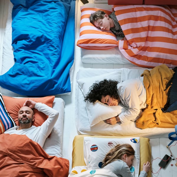 A bird’s eye view of five people asleep on different mattresses with each person having different coloured bed linen. 