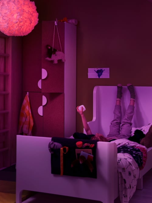 Cameră pentru copii slab iluminată, cu un bec cu LED-uri, o lampă suspendată, o telecomandă albă și un buzunar alb extensibil cu un buzunar al patului.