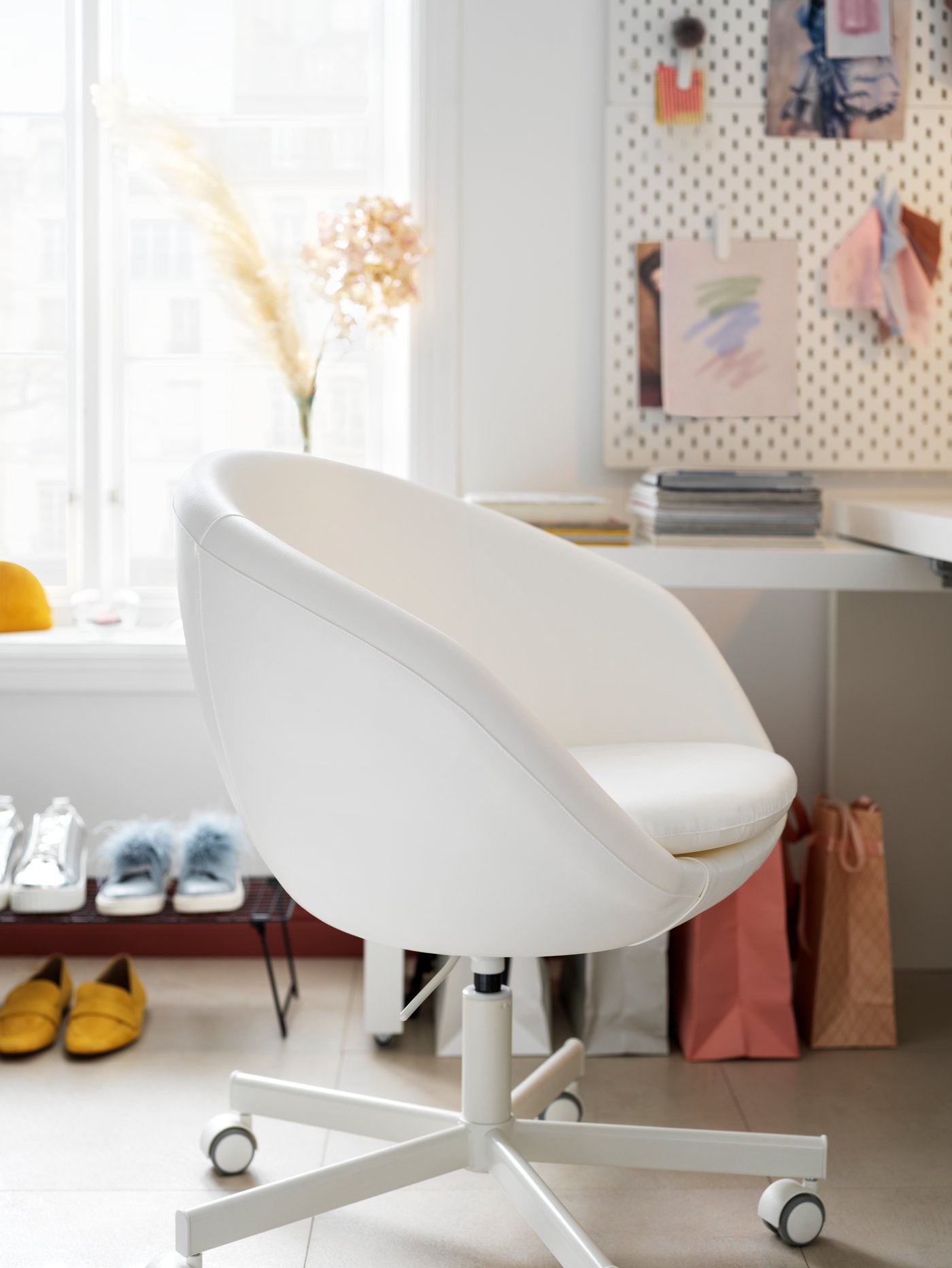 Una silla giratoria SKRUVSTA con una funda de tela revestida Ysane en blanco junto a un escritorio en una oficina doméstica. Es curvilíneo con los lados inclinados.