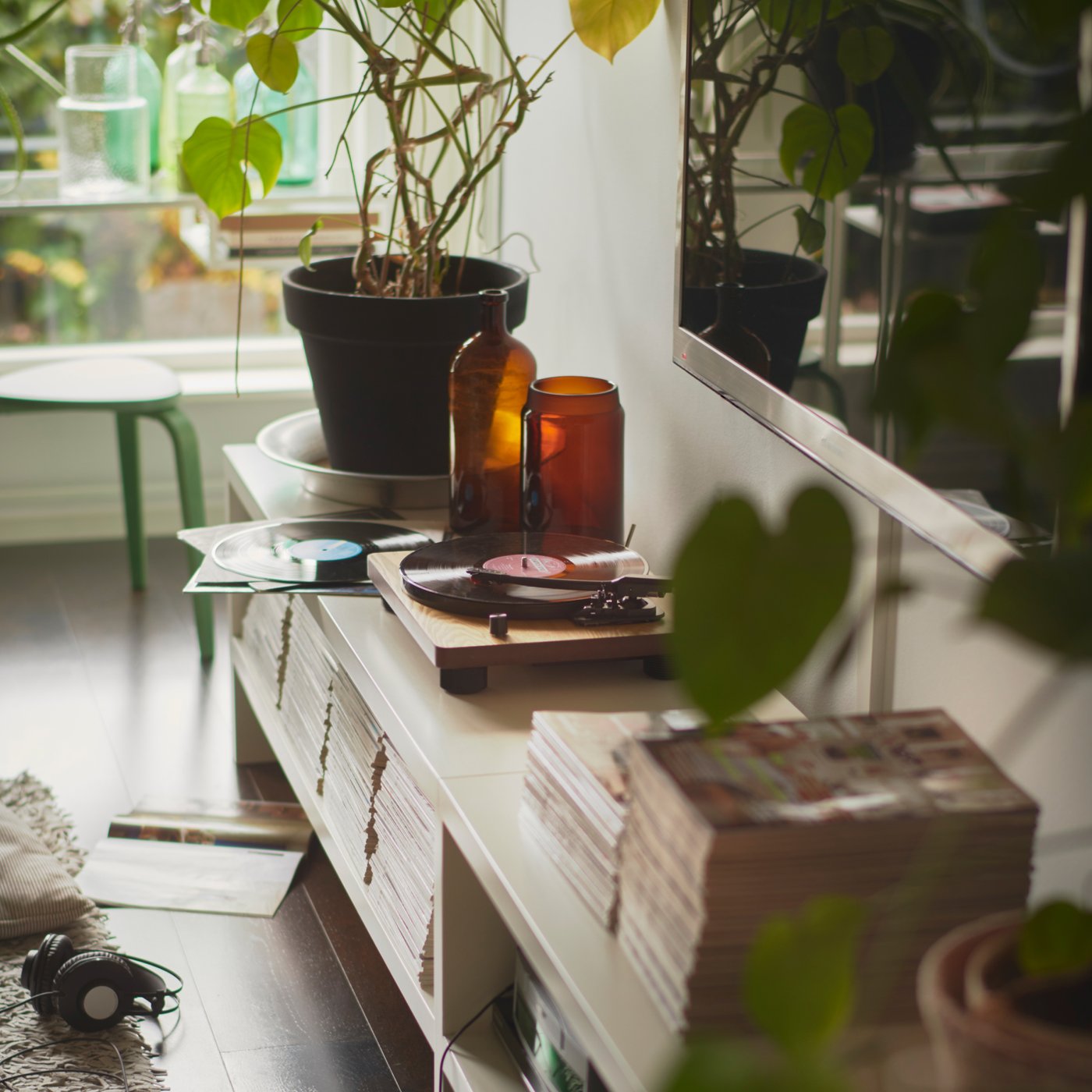 Ett vardagsrum med en TV monterad på väggen. Nedanför finns en TV-möbel med en skivspelare och en hög med tidningar.