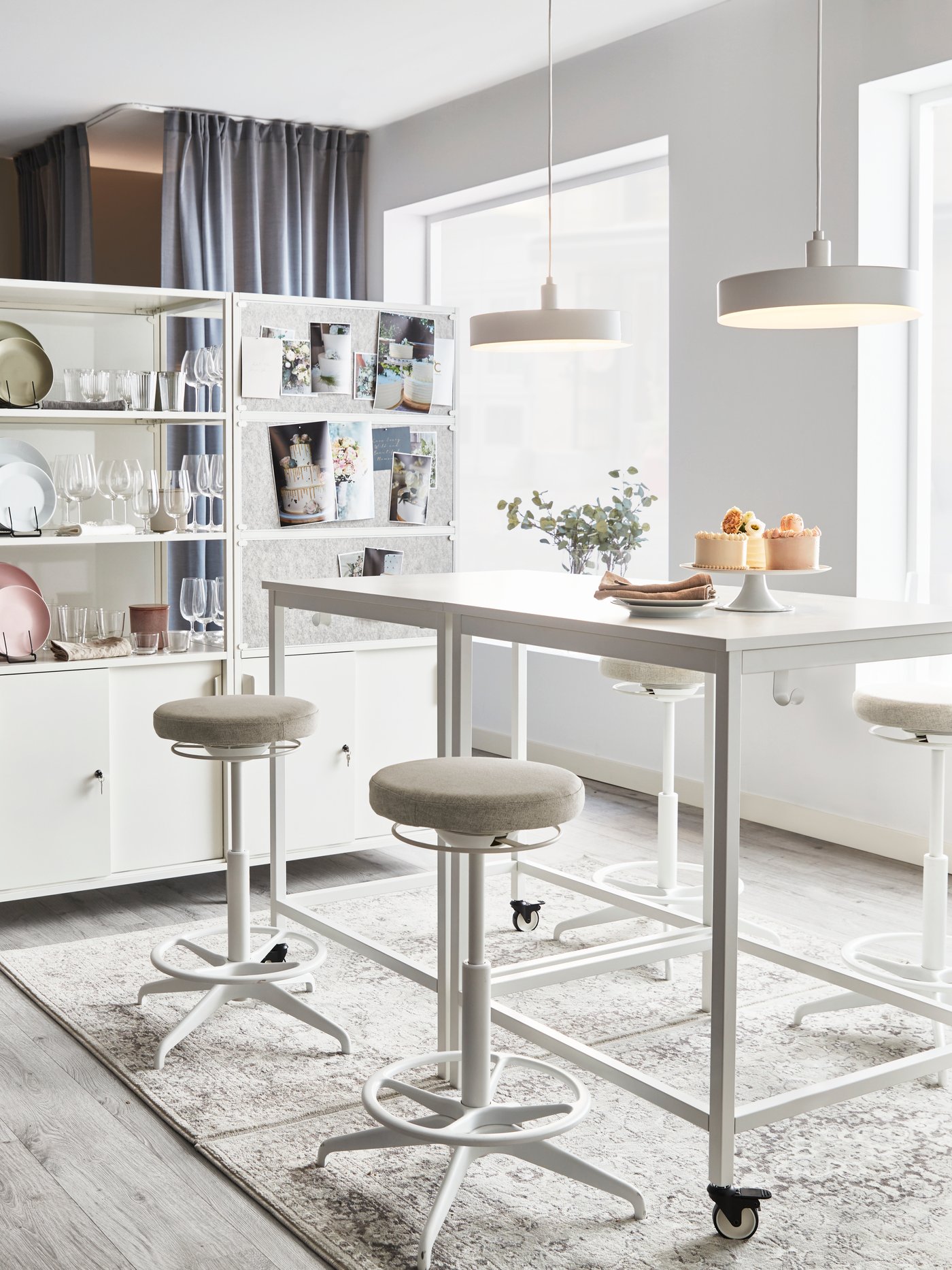 Zona de cocina con una mesa cuadrada con ruedas, dos soportes de pie/sentado, armarios con puertas correderas y lámparas colgantes.