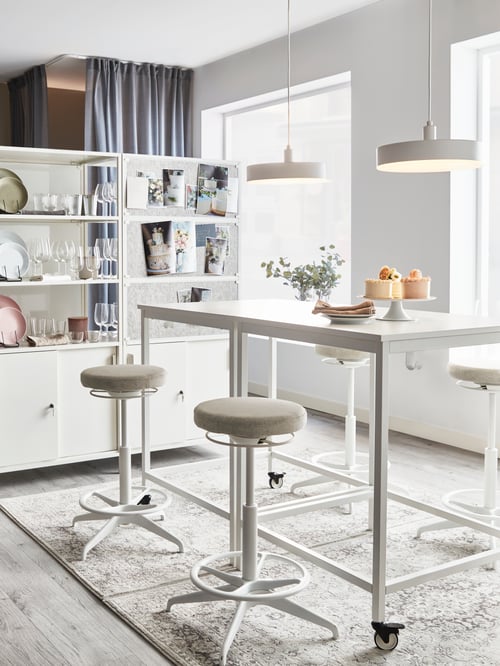 Kitchen area featuring a square table on castors, two sit stand supports, cabinets with sliding doors, and pendant lamps.