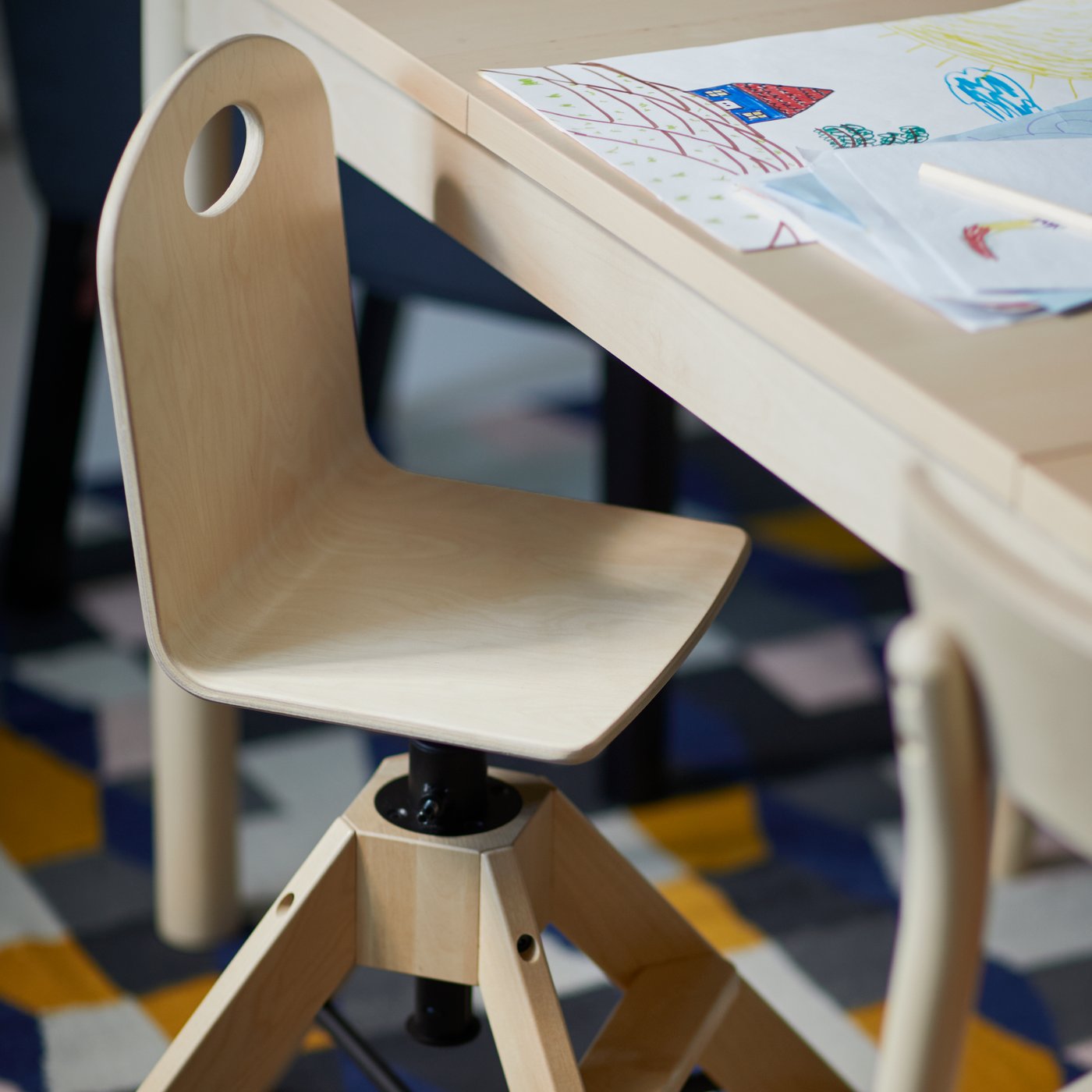 Une chaise junior en bois devant une table avec un dessin