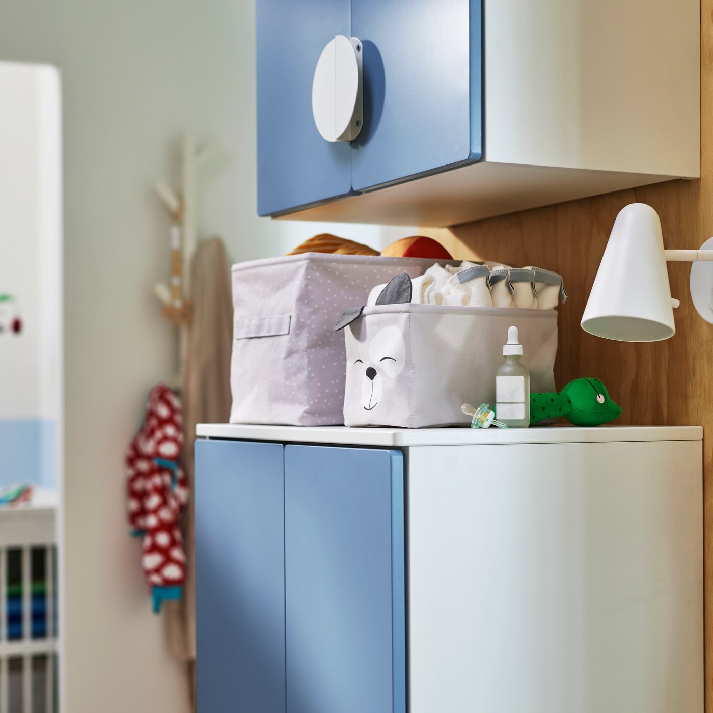 A blue SMÅSTAD wall cabinet above a blue SMÅSTAD wardrobe that has two DRÖMSLOTT storage boxes holding baby thing on the top.