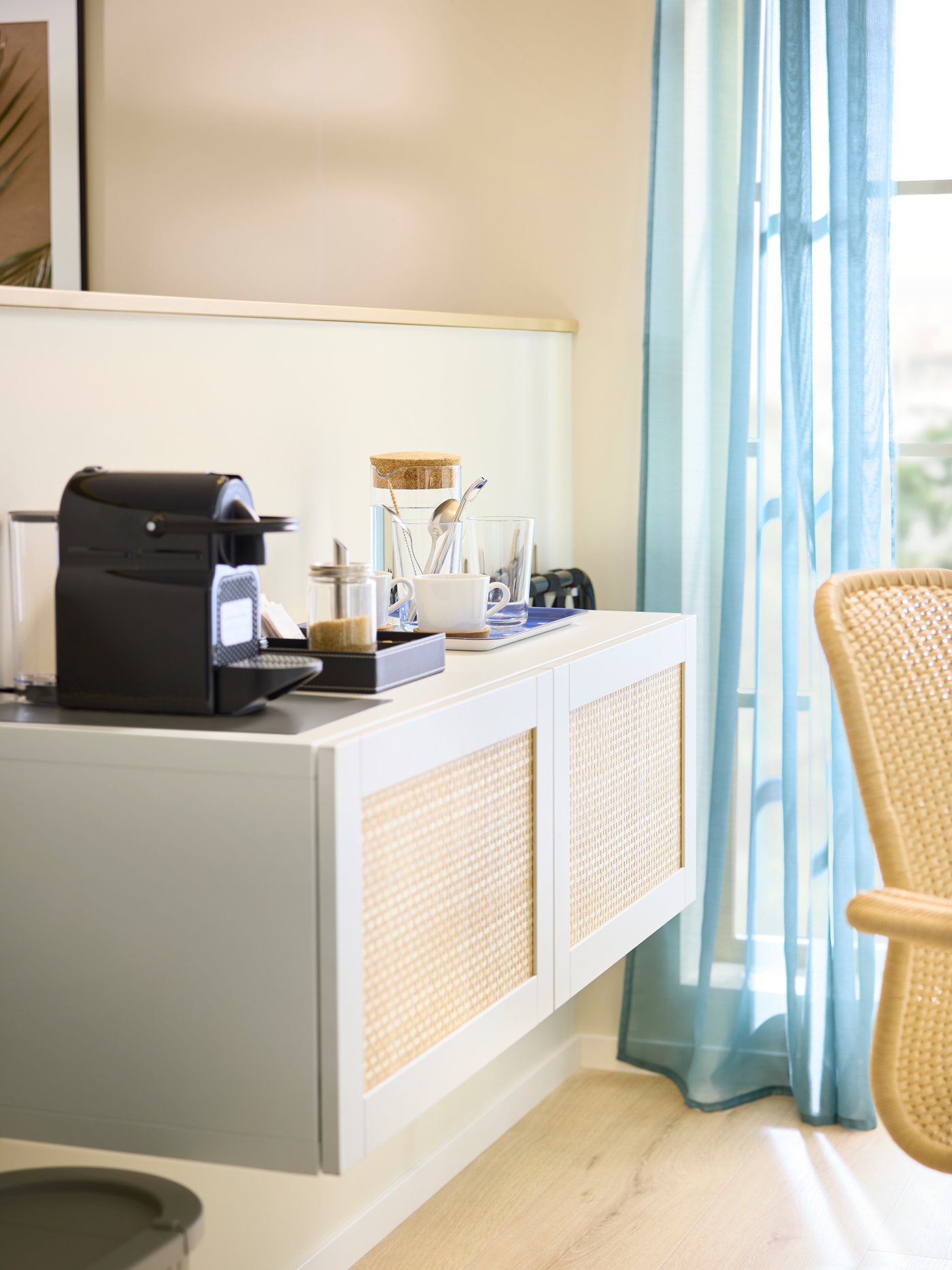 A white BESTÅ frame with STUDSVIKEN woven poplar doors is mounted on a low wall as a coffee and tea area in a hotel room.