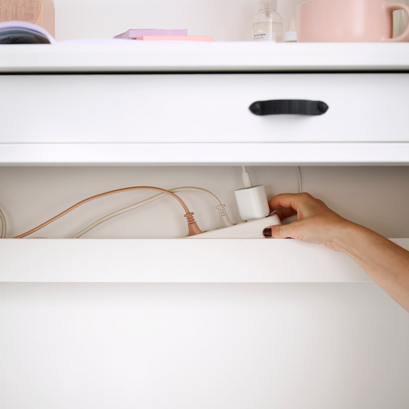 A close-up of a hand connecting a white KOPPLA 4-way socket with 2 USB ports on a desk, showing wires and devices.