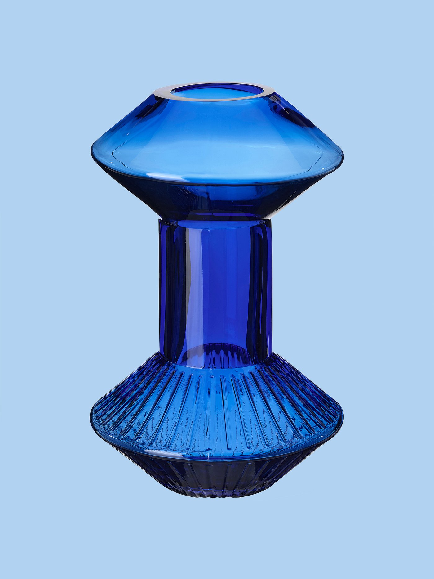 Večji del fotografije zavzema modra vaza IKEA, ki stoji pred modrim ozadjem.