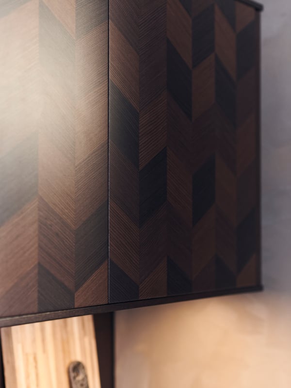 Two brown HASSLARP kitchen wall cabinet fronts with a dark wood chevron pattern against a beige wall, with lighting below.