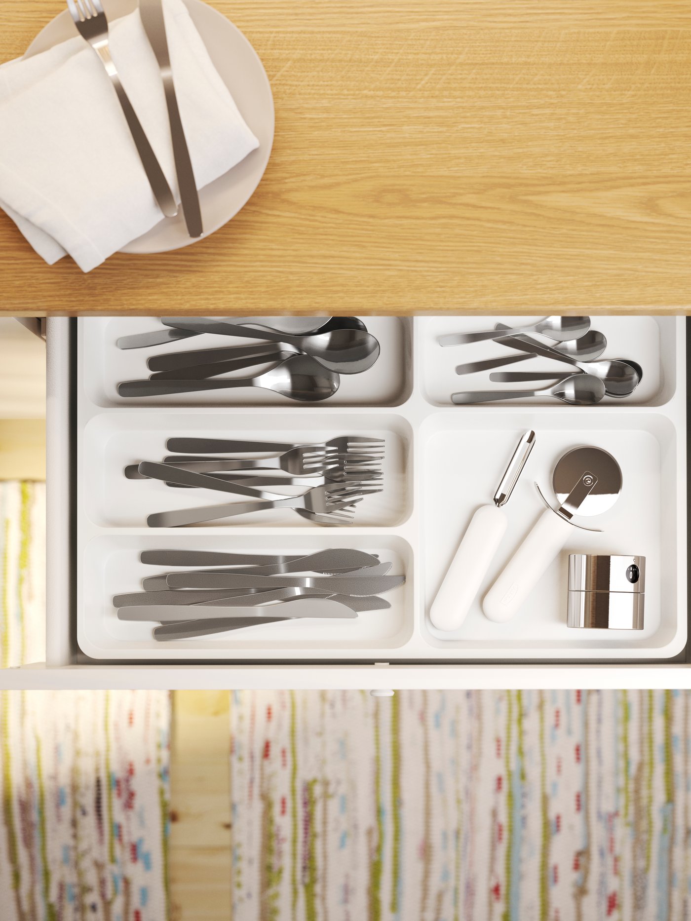 Vista de un cajón de cocina abierto con una bandeja para cubiertos gris, un juego de cubiertos con veinticuatro piezas, cortapizzas y pelapatatas.