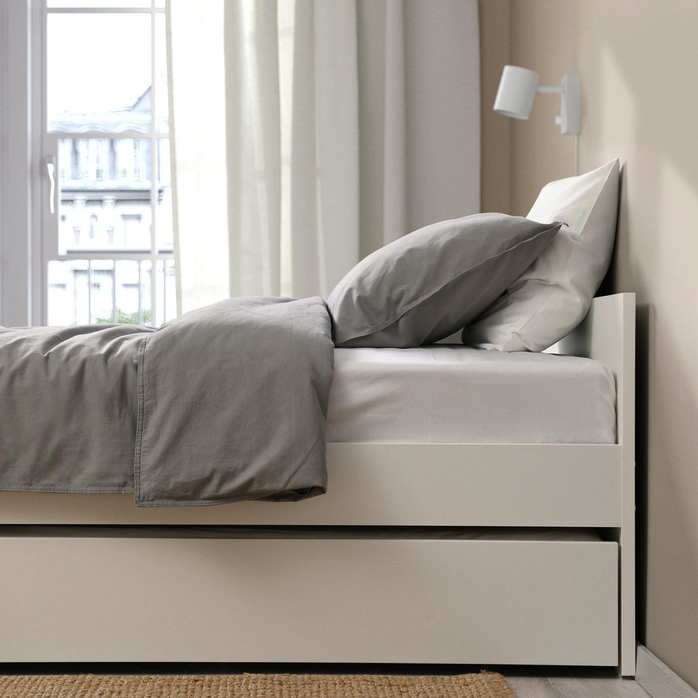 Una cama nido VIHALS con colchón y ropa de cama en gris y blanco.