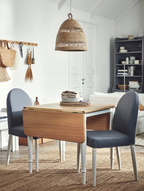 A modern dining room featuring a drop leaf table with two chairs, and a rug. A pendant lamp shade hangs over the table.
