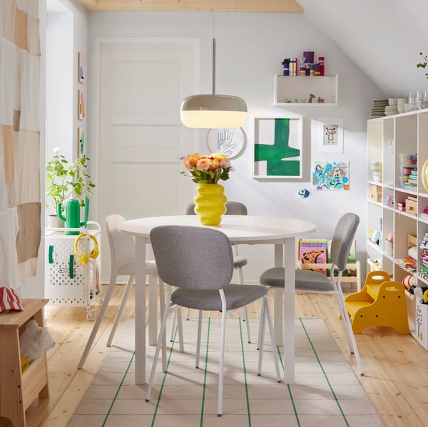 A bright dining area with a round table surrounded by four VIHALS chairs in white beige-grey, illuminated by a pendant light.