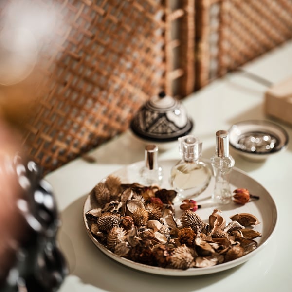Pot-pourri à la vanille FRÖFINK et trois flacons de parfum garnissant une assiette KRUSTISTEL beige clair posée sur une table blanche.