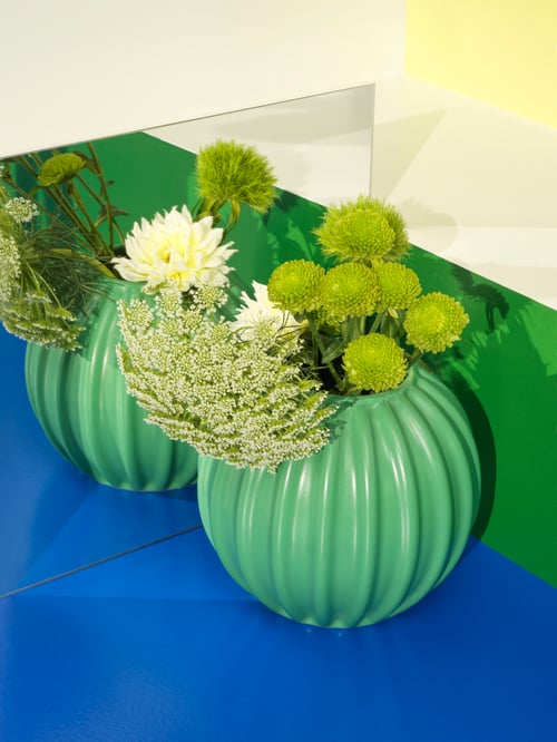 畝模様と花をあしらった丸いグリーンのSKOGSTUNDRA スコグストゥンドラ 花瓶のクローズアップ。ミラーに置いて形を映している。