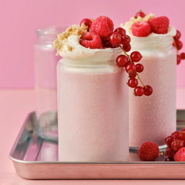 Two glass jars have LÅNGLUR fruit smoothie milkshakes and are topped with red raspberries, red currants and cookie crumbles.