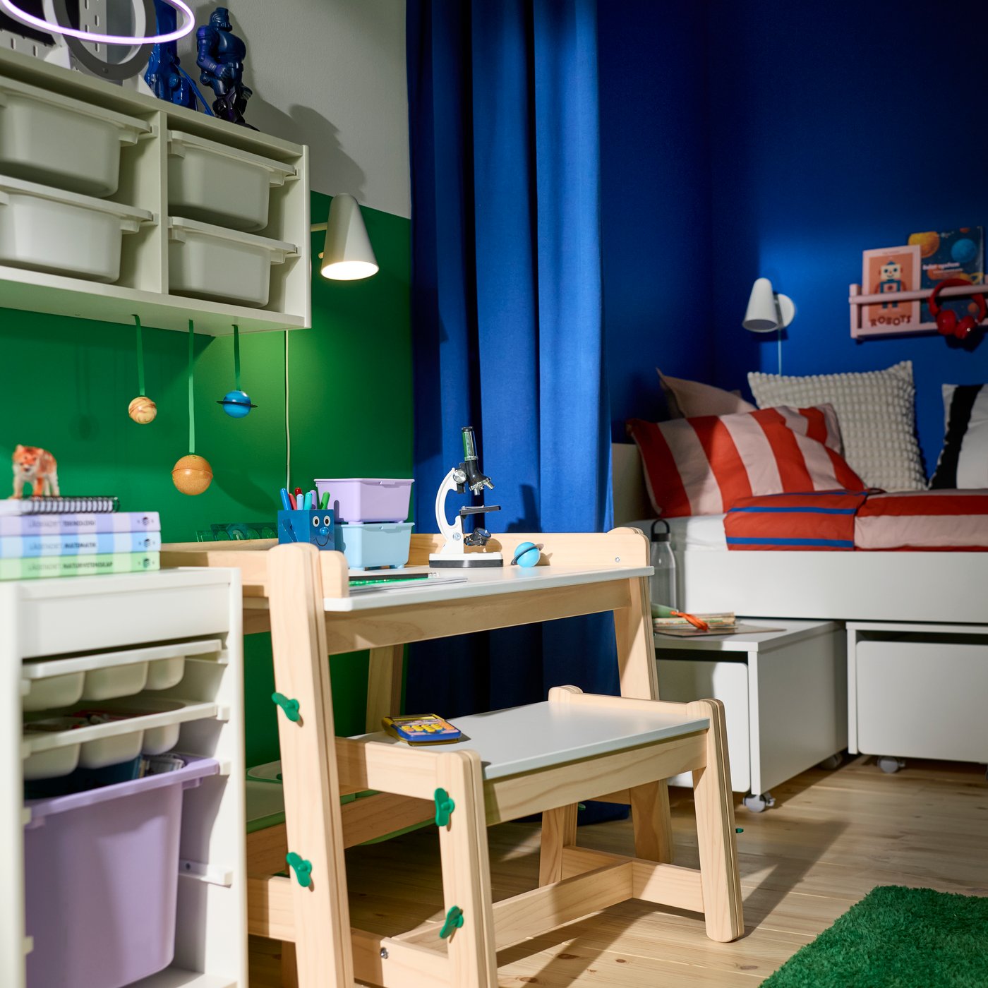 Blue GINSMOTT curtain hanging beside a children’s bench and bed in a room with shelving, storage units and study accessories.