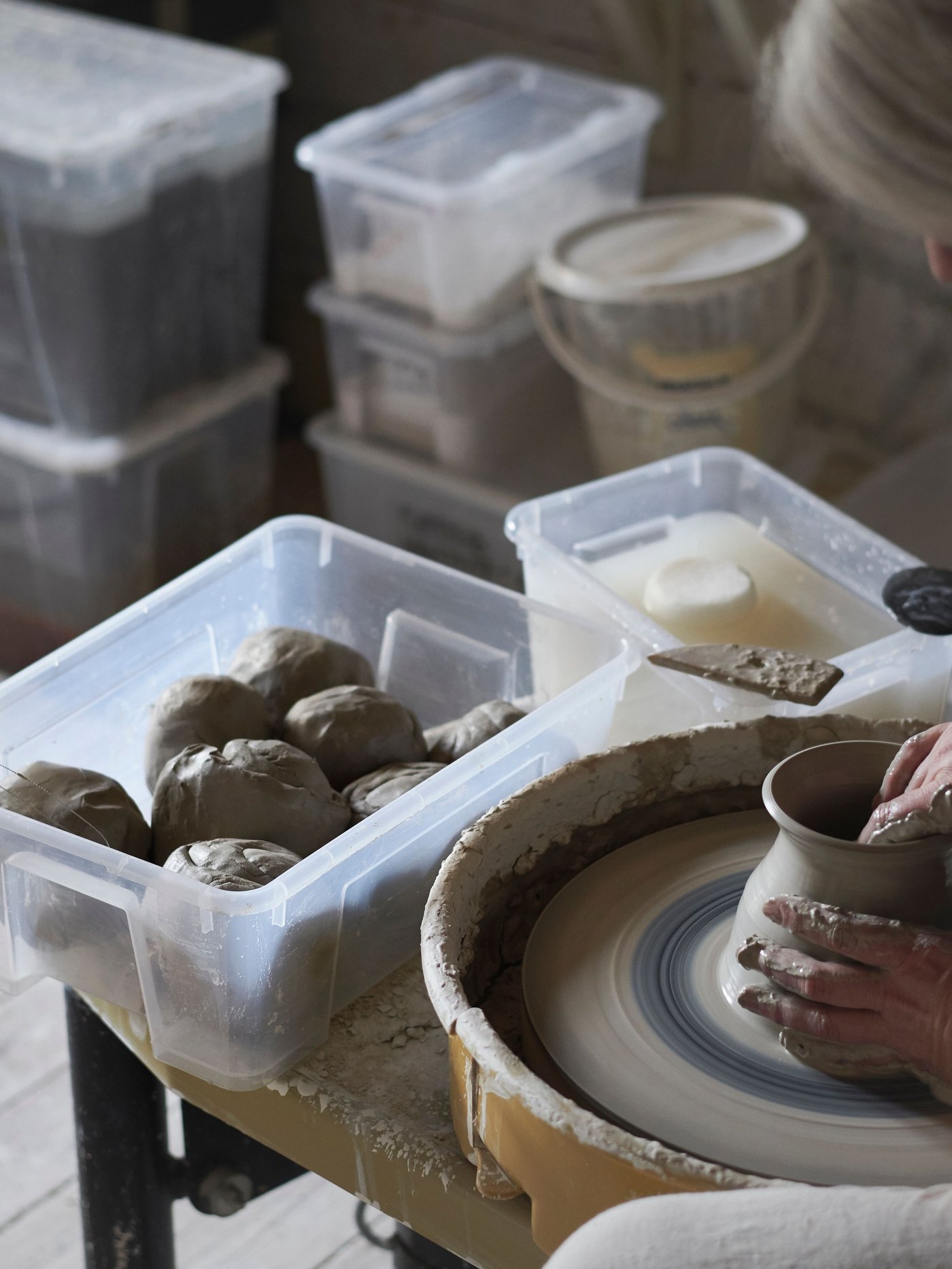 A person is making pottery using a potter’s wheel. There are SAMLA boxes on the bench and stacked on the floor.