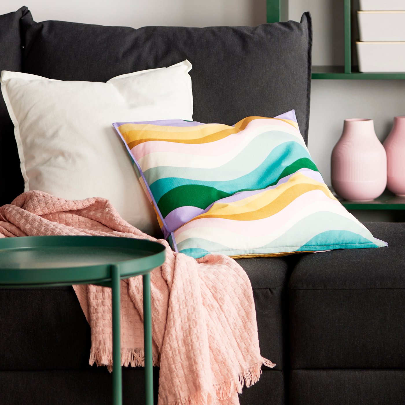 Dark sofa which has two cushions on it, the other one is white and the other one has multicolor MYGGBLOMSTER cushion cover.
