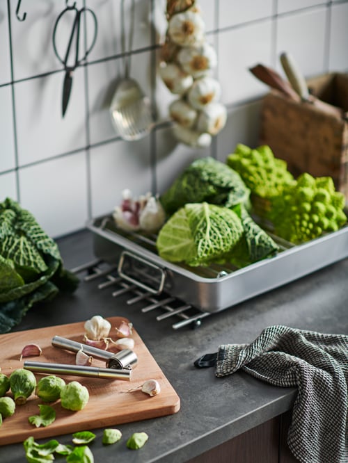 A kitchen worktop with savoy cabbage in a KONCIS roasting tin next to a chopping board with garlic and a KONCIS garlic press.