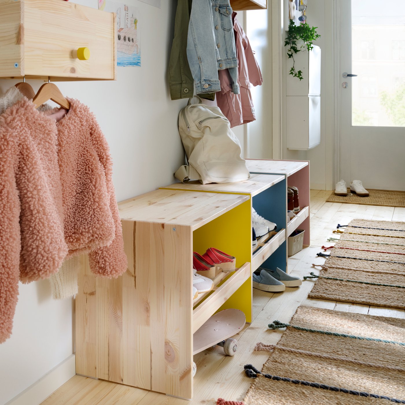 The left wall of a family hallway with RAGGBERG benches and coat racks in pine, with details painted in bright colours.