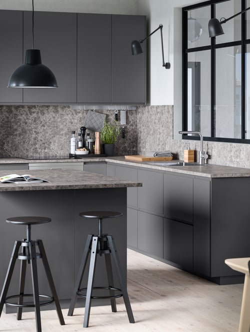 Kitchen with dark grey base cabinets, wall cabinet, black bar stools, black wall lamp and pendant lamp, worktop. 