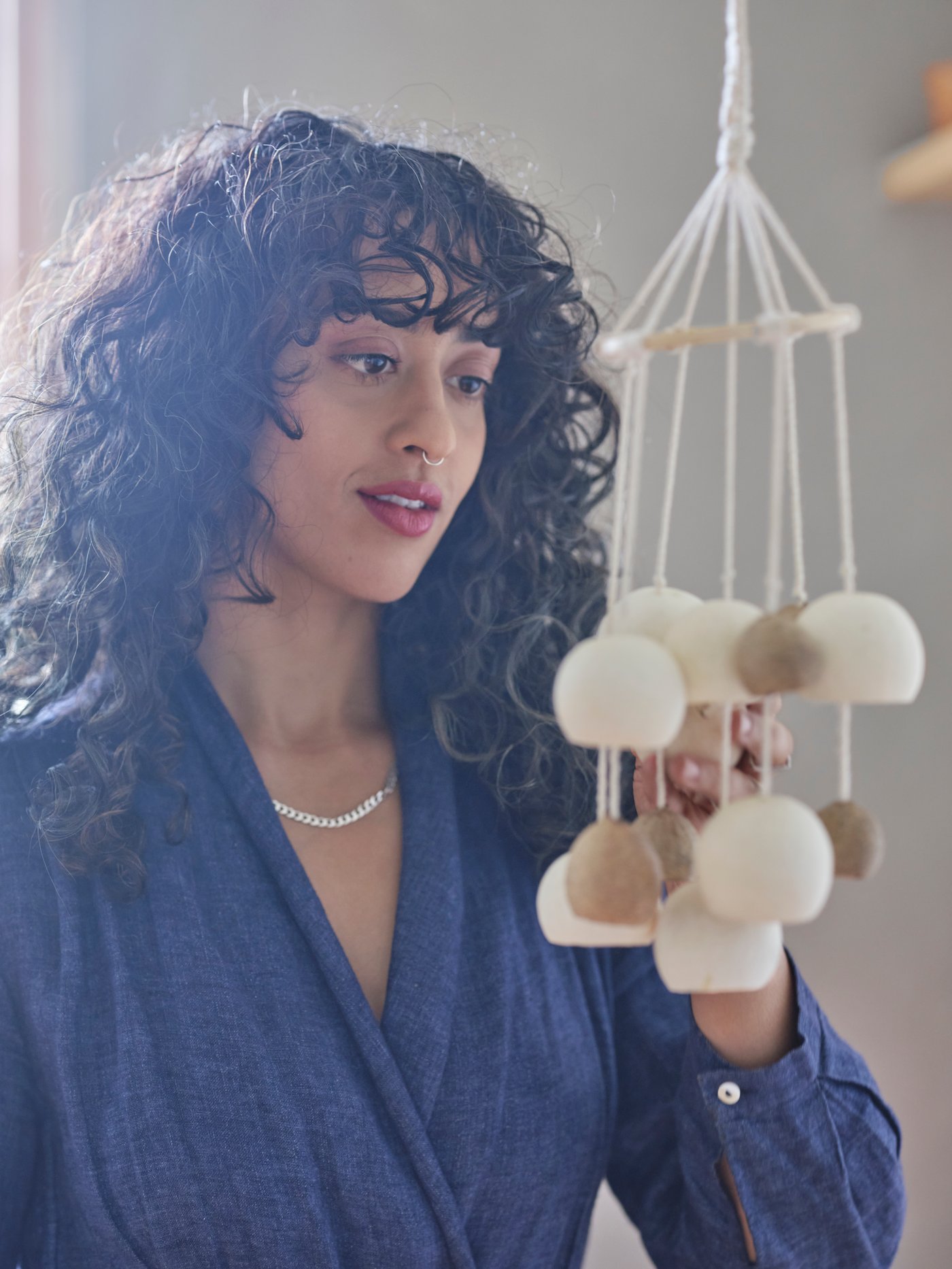 A woman in a blue shirt looking at a VÅRDANDE hanging decoration of dried bell cups on cotton strings.