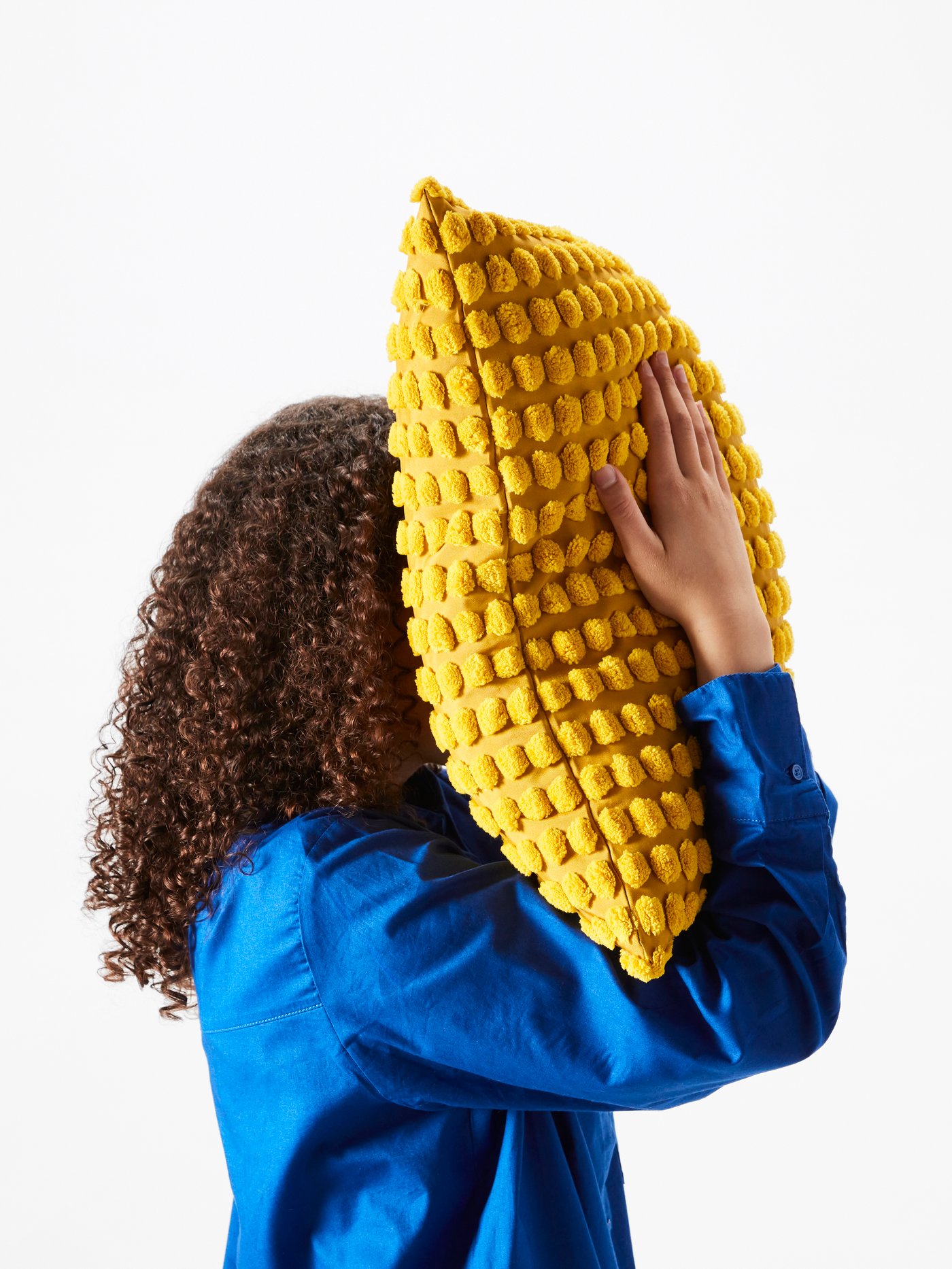 Una persona tiene in mano un cuscino con fodera giallo SVARTPOPPEL e lo stringe verso il viso.